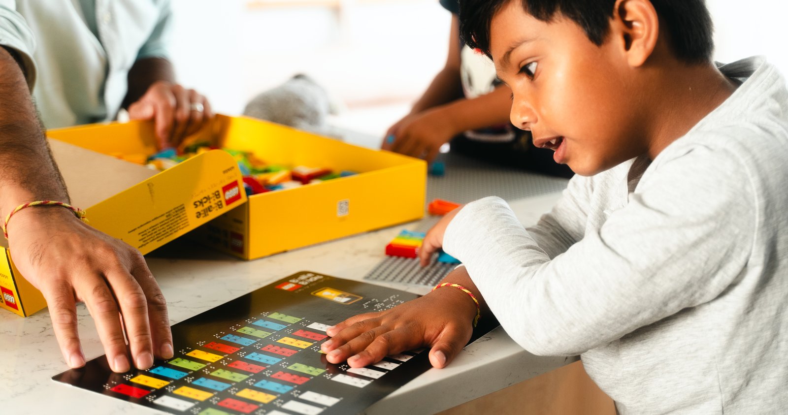 A child exploring LEGO Braille Bricks with an adult